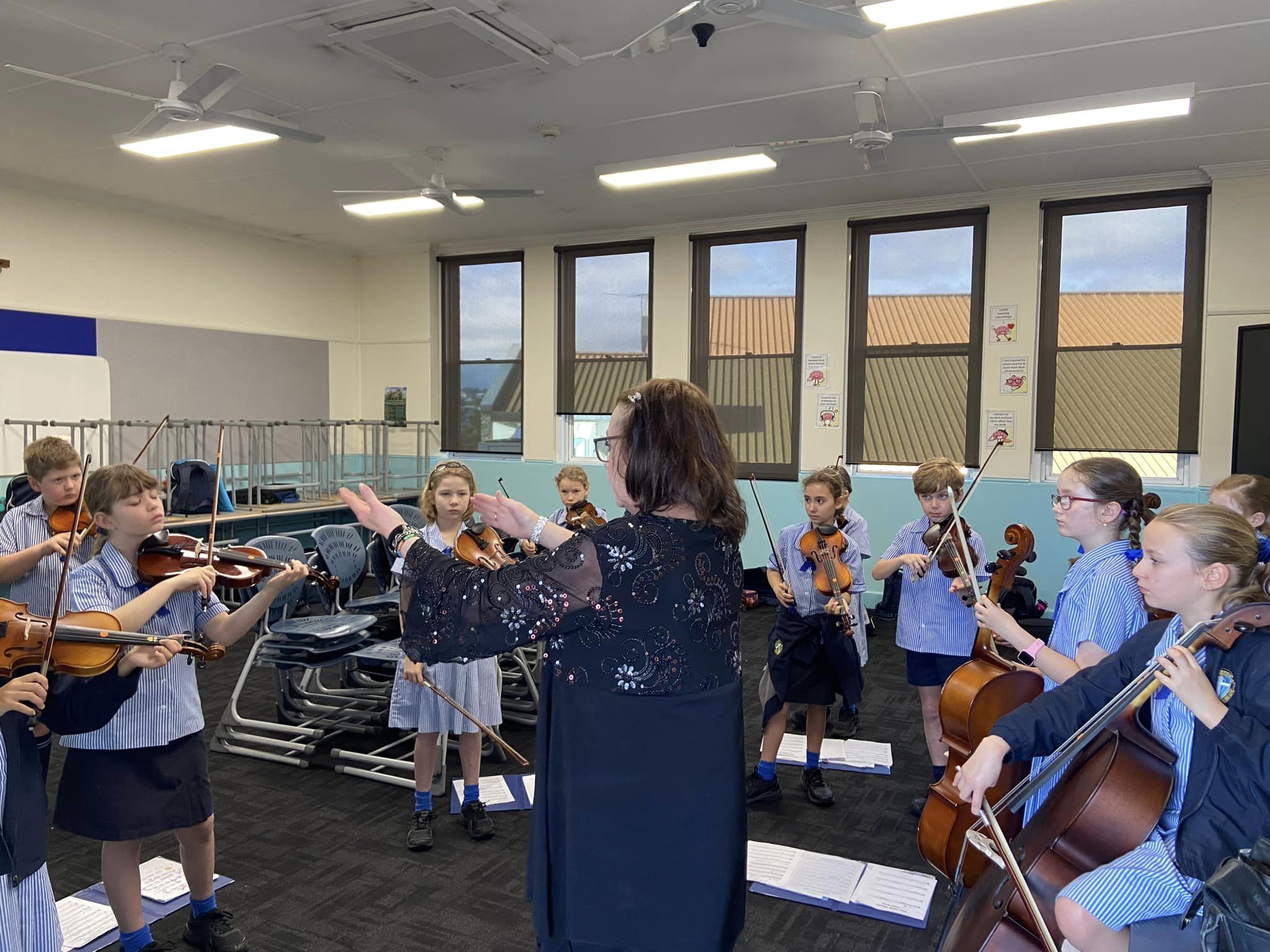 Students playing string instruments together under teacher guidance, highlighting music education, collaboration and creative learning within the primary school environment